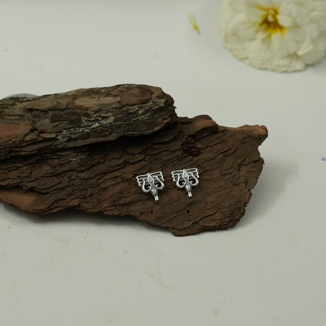 My Guru Ji silver-toned brass stud earrings featuring Trishul and Damru Lord Shiva symbols on a piece of tree bark.