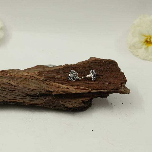 My Guru Ji silver-toned brass stud earrings featuring Lord Shiva Trishul and Damru symbols on a rustic wooden surface.