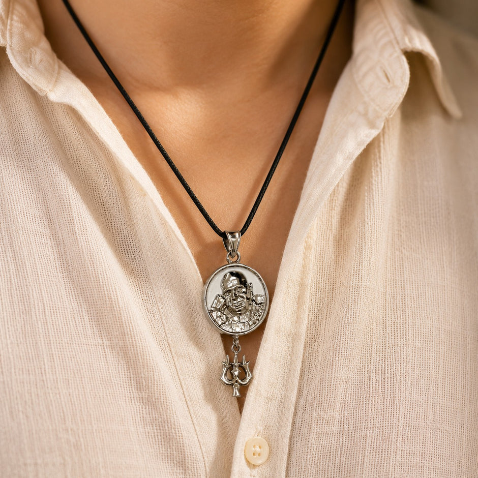 My Guru Ji Shukrana Trishul pendant in silver-finished brass worn on a black cord against a beige linen shirt.