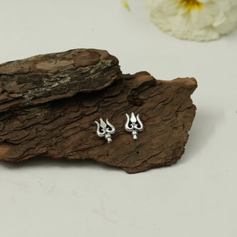 My Guru Ji silver finish brass Trishul stud earrings featuring Lord Shiva symbol design on a rustic wood background